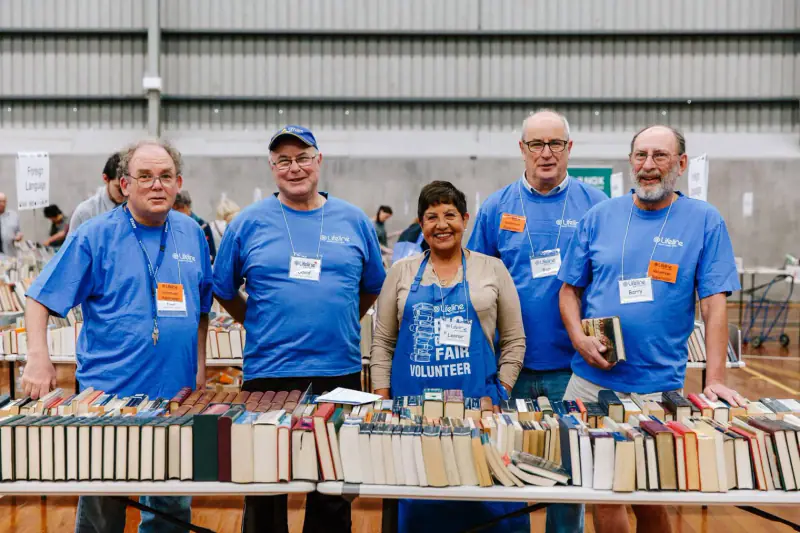 Five Lifeline volunteers in Big Book Fair shirts standing behind a table of second-hand books