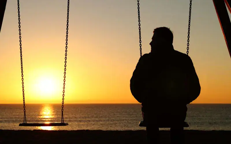 A person sitting on a swing watching the sunrise over the ocean